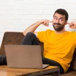 Hombre con su laptop en una habitación que cubre ambas orejas con las manos